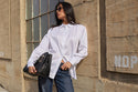 Woman in a white shirt and jeans holding a black bag against a textured wall.
